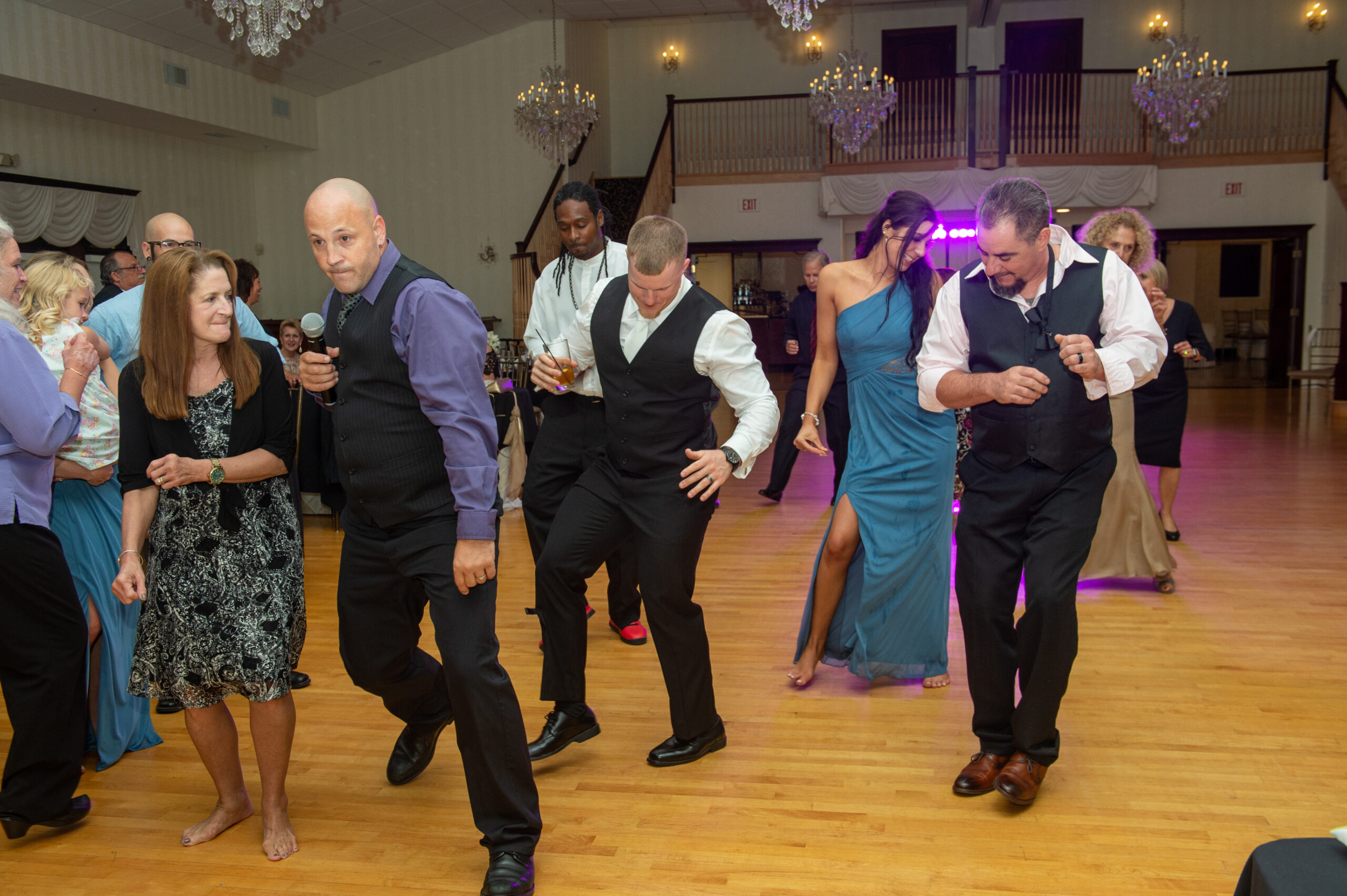 Wedding DJ with a microphone leading guests in a line dance under crystal chandeliers at Cascade in Hamden CT