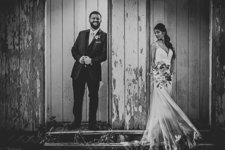 Bride and groom standing in front of weathered barn doors with peeling paint at Powder Ridge Mountain Park in Middlefield CT, black and white