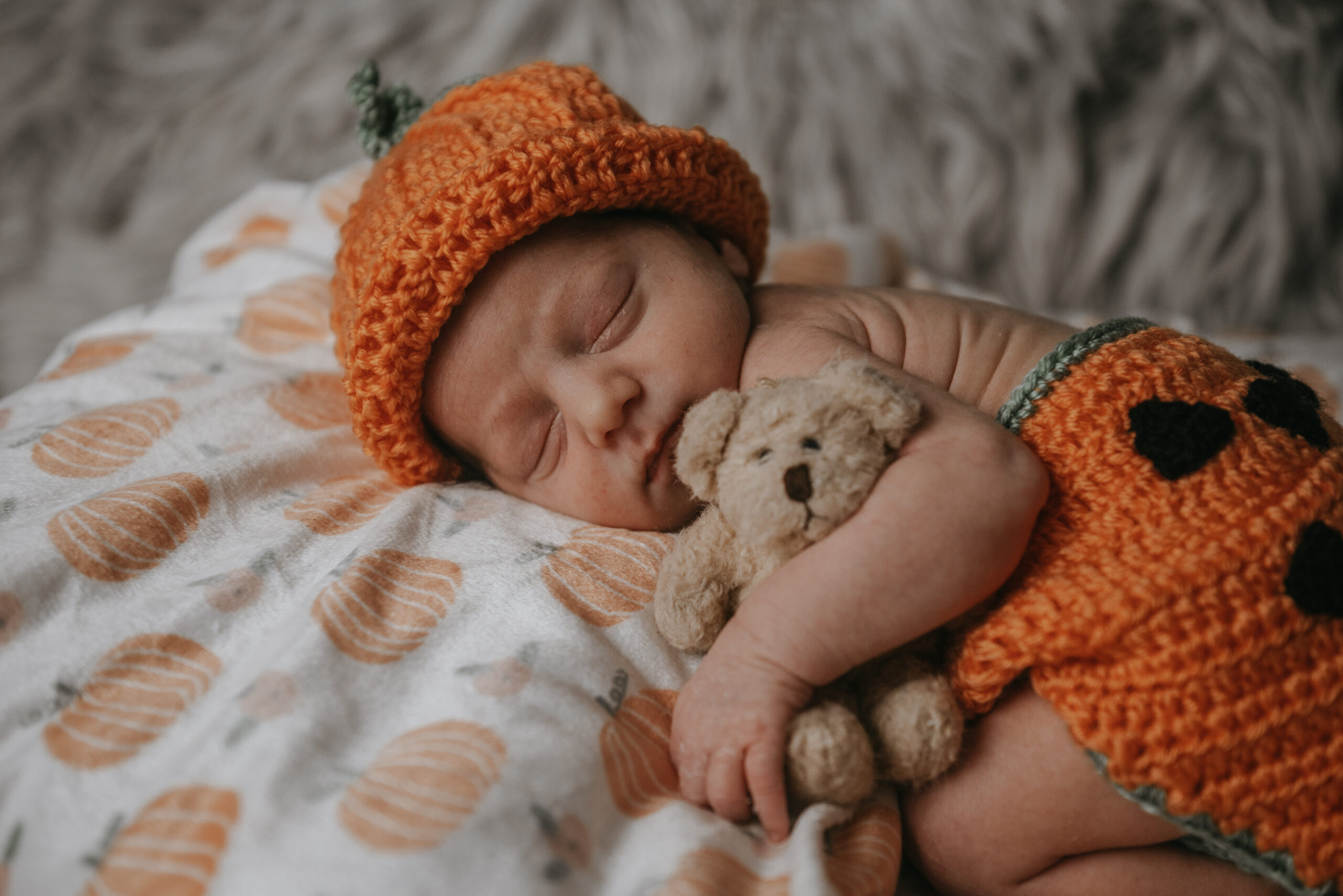 Newborn baby in orange knit hat with stuffed bear during a Connecticut newborn session