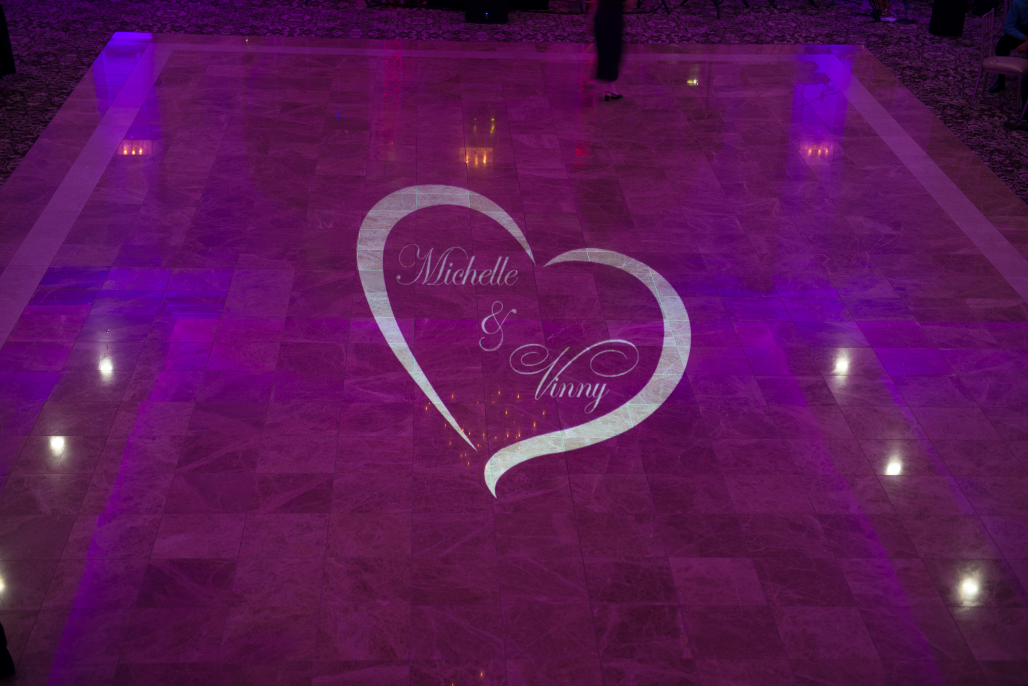 Custom heart monogram with couple's names projected on the dance floor with purple uplighting at Aria in Prospect CT