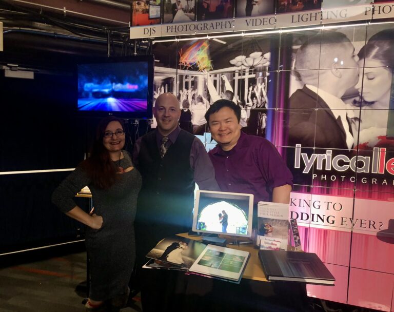 Connie, Dave, and Matt from Lyrical Lens Events at their booth with wedding albums and portfolio display at a Jenks Productions bridal show in Connecticut