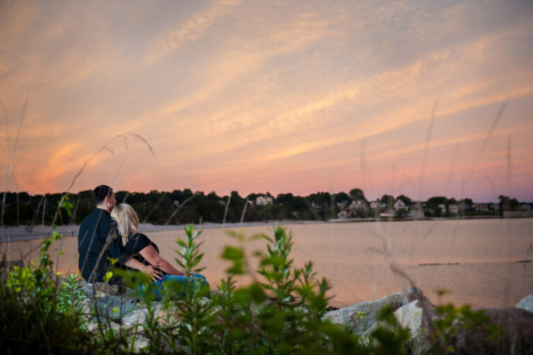 Engaged couple sitting on beach rocks at sunset in Niantic Connecticut during their engagement photography session