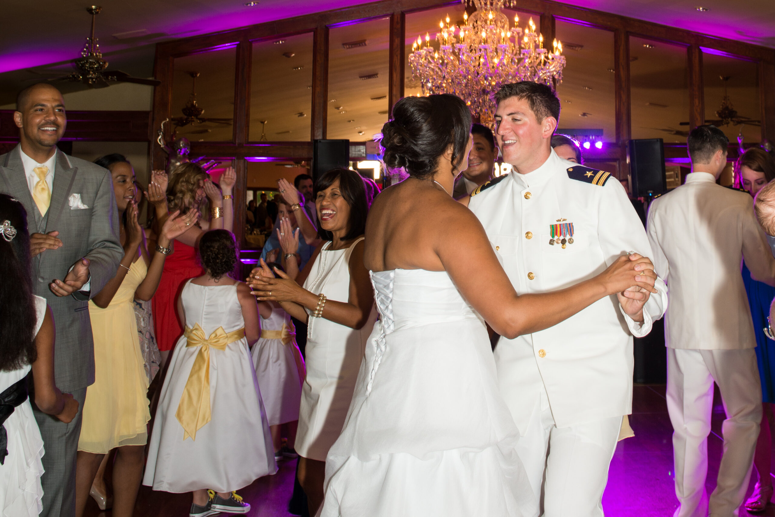 Bride and groom in military dress whites dancing surrounded by clapping guests under purple uplighting at St. Clements Castle in Portland CT