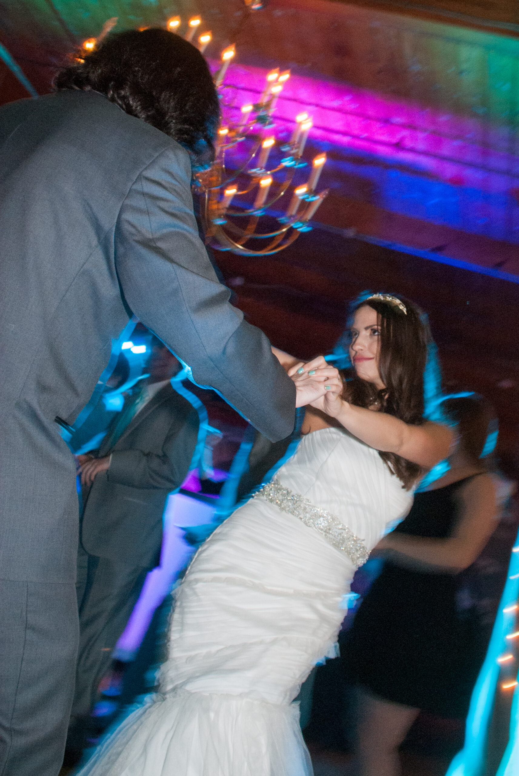 Bride dancing with groom under a chandelier with colorful uplighting at the Carousel Museum in Bristol CT