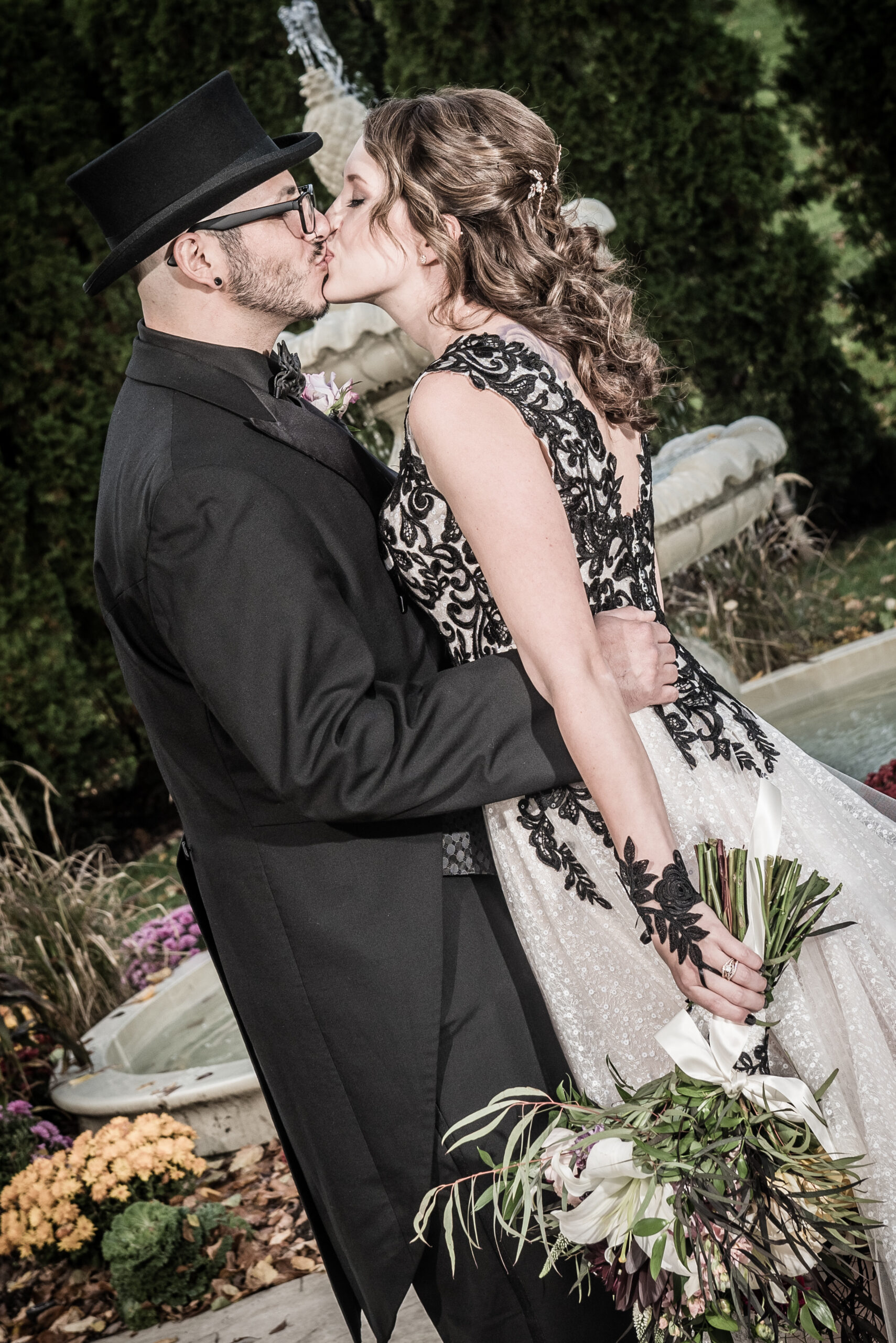 Bride in black lace gown and groom in top hat kissing by a fountain at the Waterview in Monroe CT